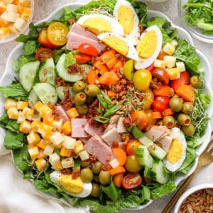 Top down shot of a large plate of chef salad with hard boiled eggs, cheese, ham, carrots and sesame seeds.