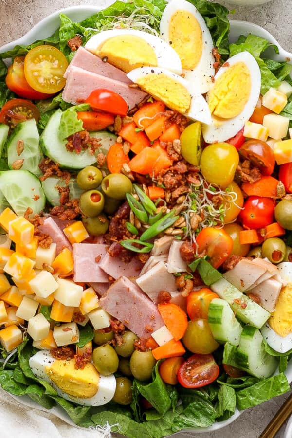 Top down shot of a large plate of chef salad with hard boiled eggs, cheese, ham, carrots and sesame seeds.