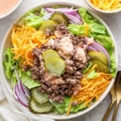 Top down shot of a big bowl of big mac salad with lettuce, shredded cheese, onions and burger pickles with big mac sauce on top.