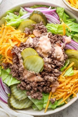 Top down shot of a big bowl of big mac salad with lettuce, shredded cheese, onions and burger pickles with big mac sauce on top.