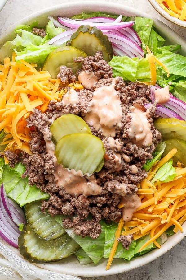 Top down shot of a big bowl of big mac salad with lettuce, shredded cheese, onions and burger pickles with big mac sauce on top.