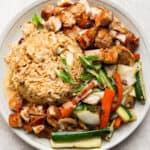 A plate of hibachi chicken with some vegetables and fried rice, green onion and yum yum sauce drizzled on top.