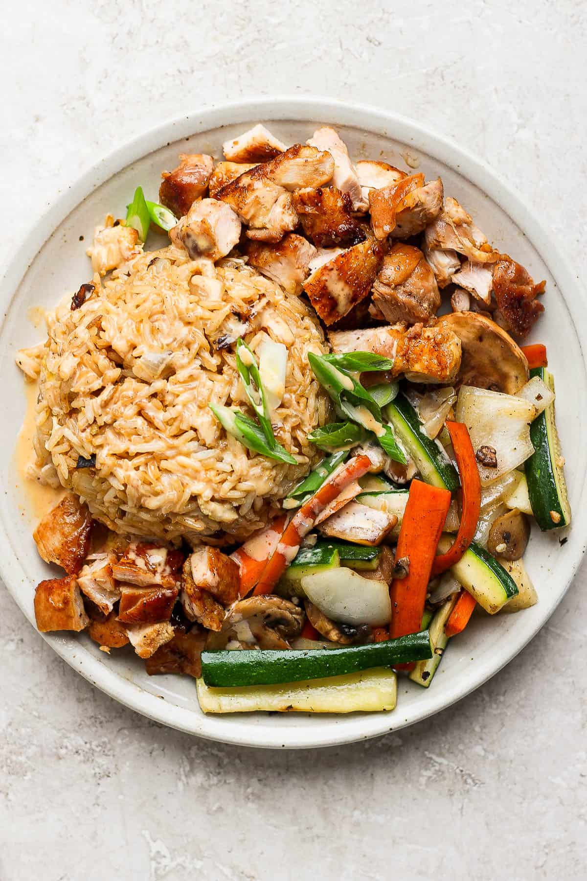 A plate of chicken hibachi with veggies, fried rice, and sauce on top.