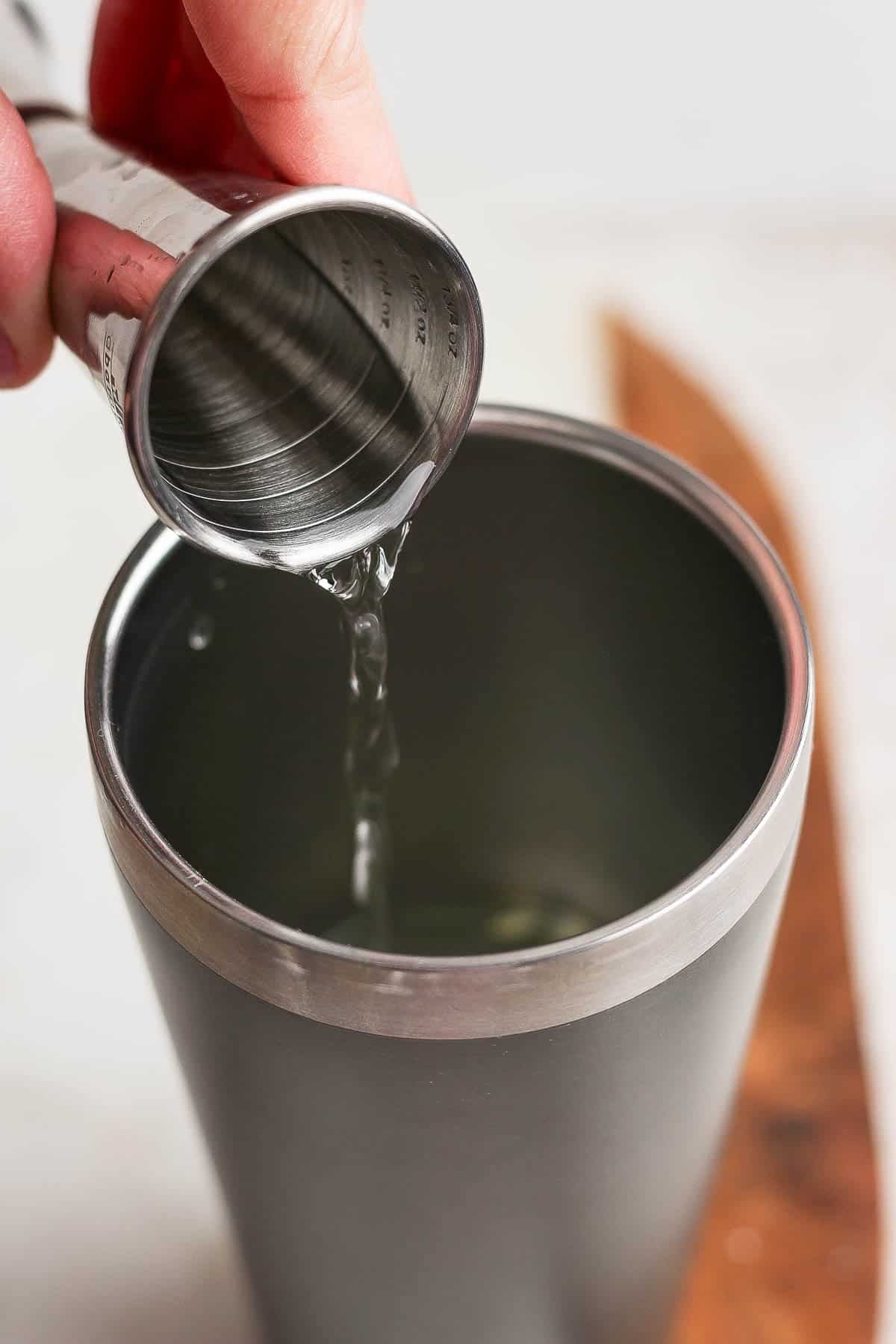 All of the pickle margarita ingredients being poured into a cocktail shaker.