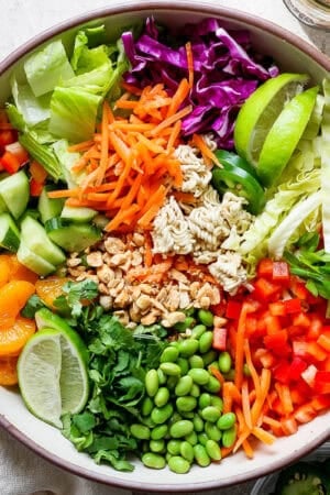 Top down shot of a bowl of ramen noodle salad with carrots, cabbage, cucumber, oranges, edamame and bell pepper.
