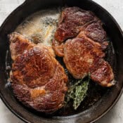 Top down shot of two ribeye steaks cooking in a cast iron skillet with melted butter and fresh thyme.