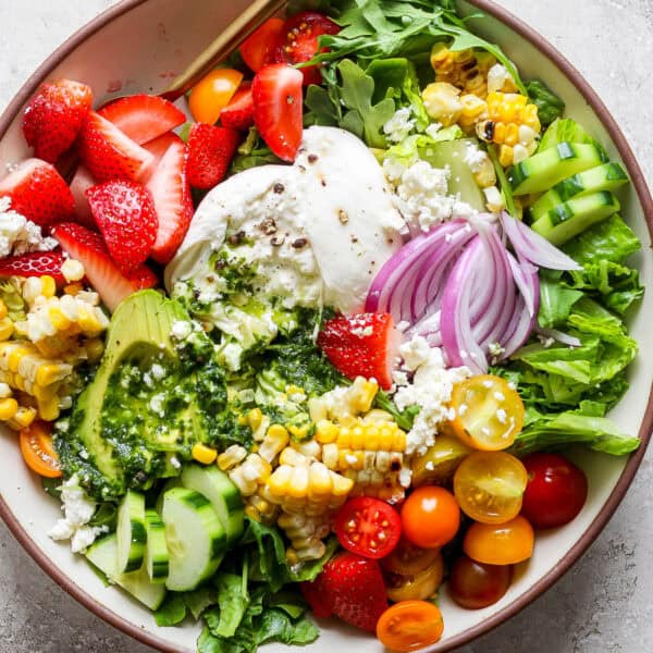 Top down shot of a big bowl of summer salad with grilled corn, burrata, basil vinaigrette, strawberries, avocado and tomatoes.