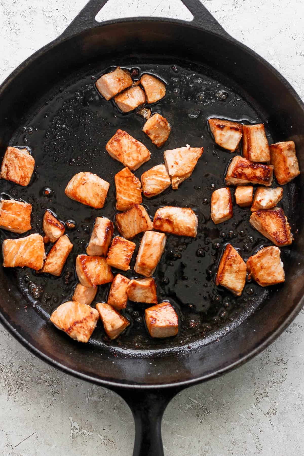 Seasoned salmon pieces in a large cast iron skillet.