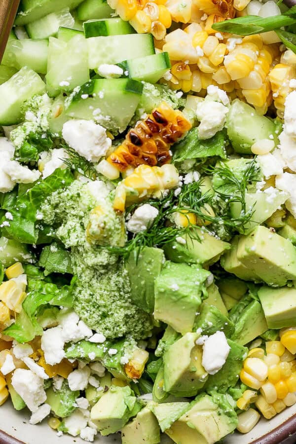 Top down shot of a big bowl of chopped avocado salad with grilled corn, feta, dill and green onion.