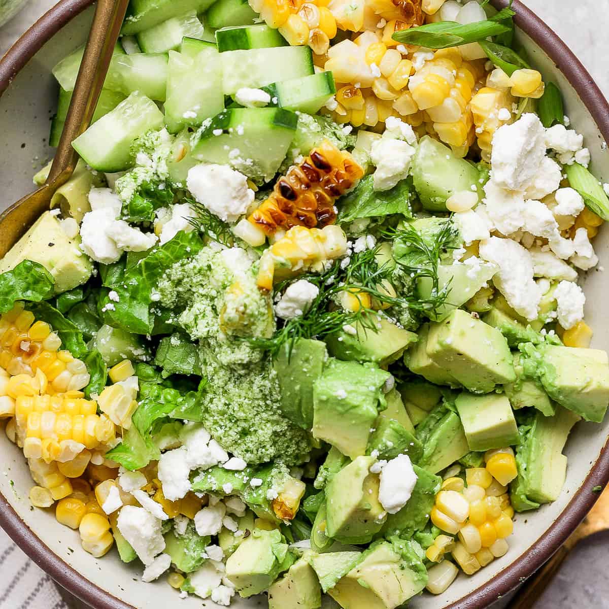 Top down shot of a big bowl of chopped avocado salad with grilled corn, feta, dill and green onion.