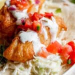 A small piece of beer battered fish on a tortilla with cilantro lime sauce and pico de gallo.