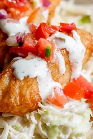 A small piece of beer battered fish on a tortilla with cilantro lime sauce and pico de gallo.