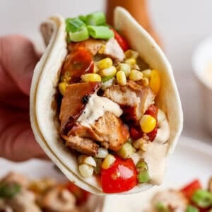 Someone holding a Blackstone chicken taco with cut up chicken, corn, tomatoes and a chipotle lime sauce.