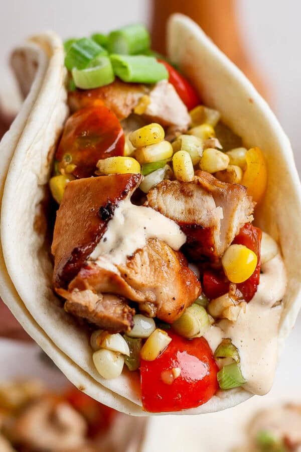 Someone holding a Blackstone chicken taco with cut up chicken, corn, tomatoes and a chipotle lime sauce.