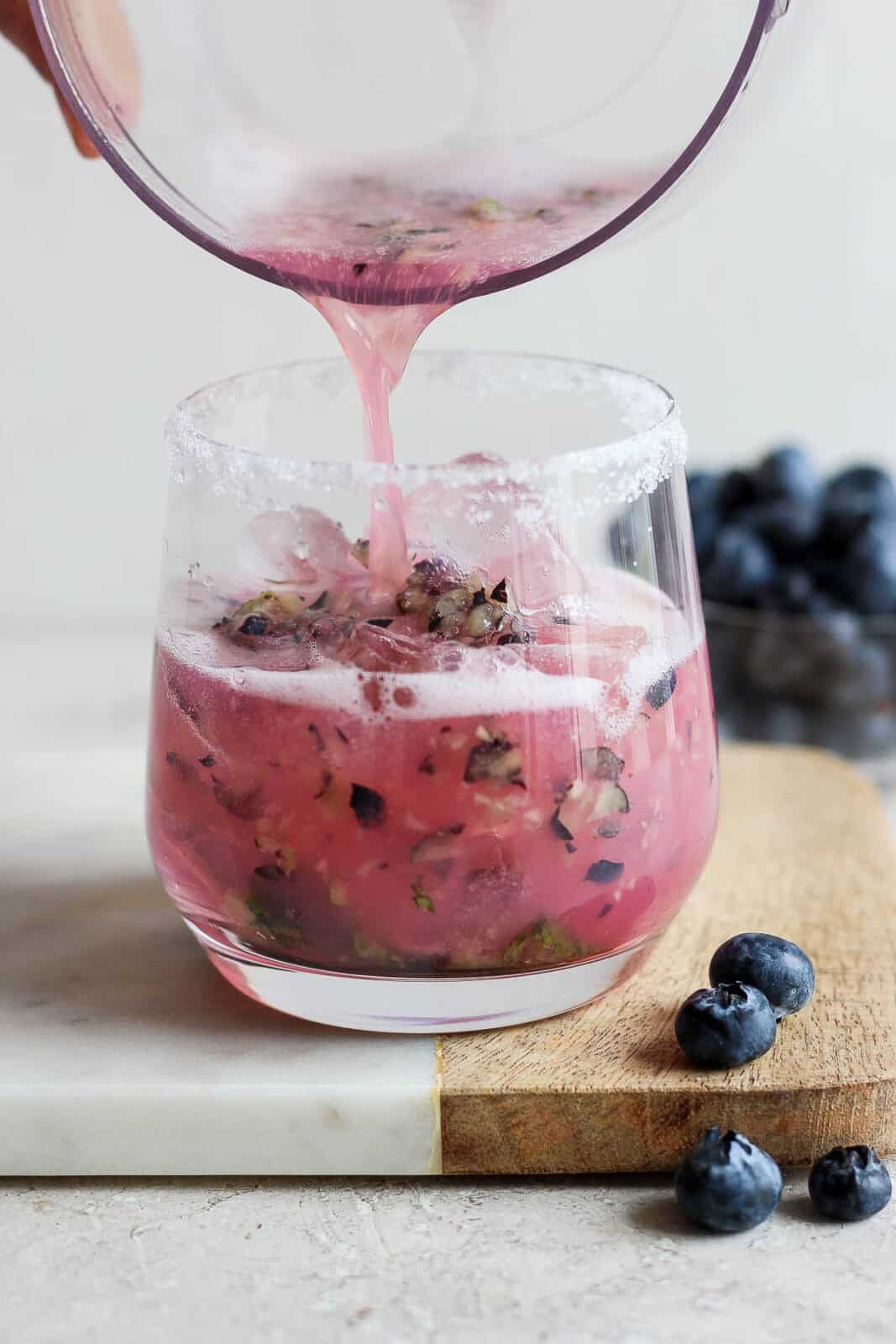 Blueberry mojito mix being poured into a sugar rimmed glass.