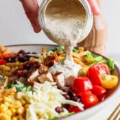 Someone pouring chipotle ranch dressing on top of a big bowl of tex mex salad.