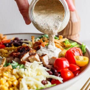 Someone pouring chipotle ranch dressing on top of a big bowl of tex mex salad.