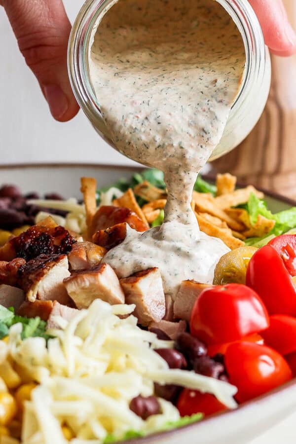 Someone pouring chipotle ranch dressing on top of a big bowl of tex mex salad.