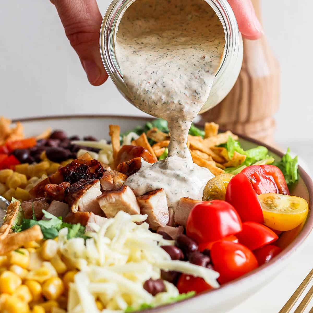 Someone pouring chipotle ranch dressing on top of a big bowl of tex mex salad.