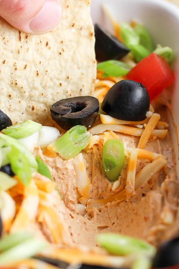 Side angle shot of someone using a tortilla chip to scoop out some taco dip from a casserole dish.