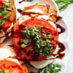 Top down shot of a piece of grilled chicken caprese with chopped fresh basil on top and balsamic glaze.