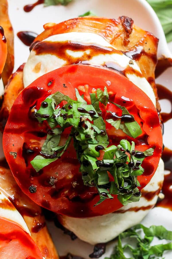 Top down shot of a piece of grilled chicken caprese with chopped fresh basil on top and balsamic glaze.