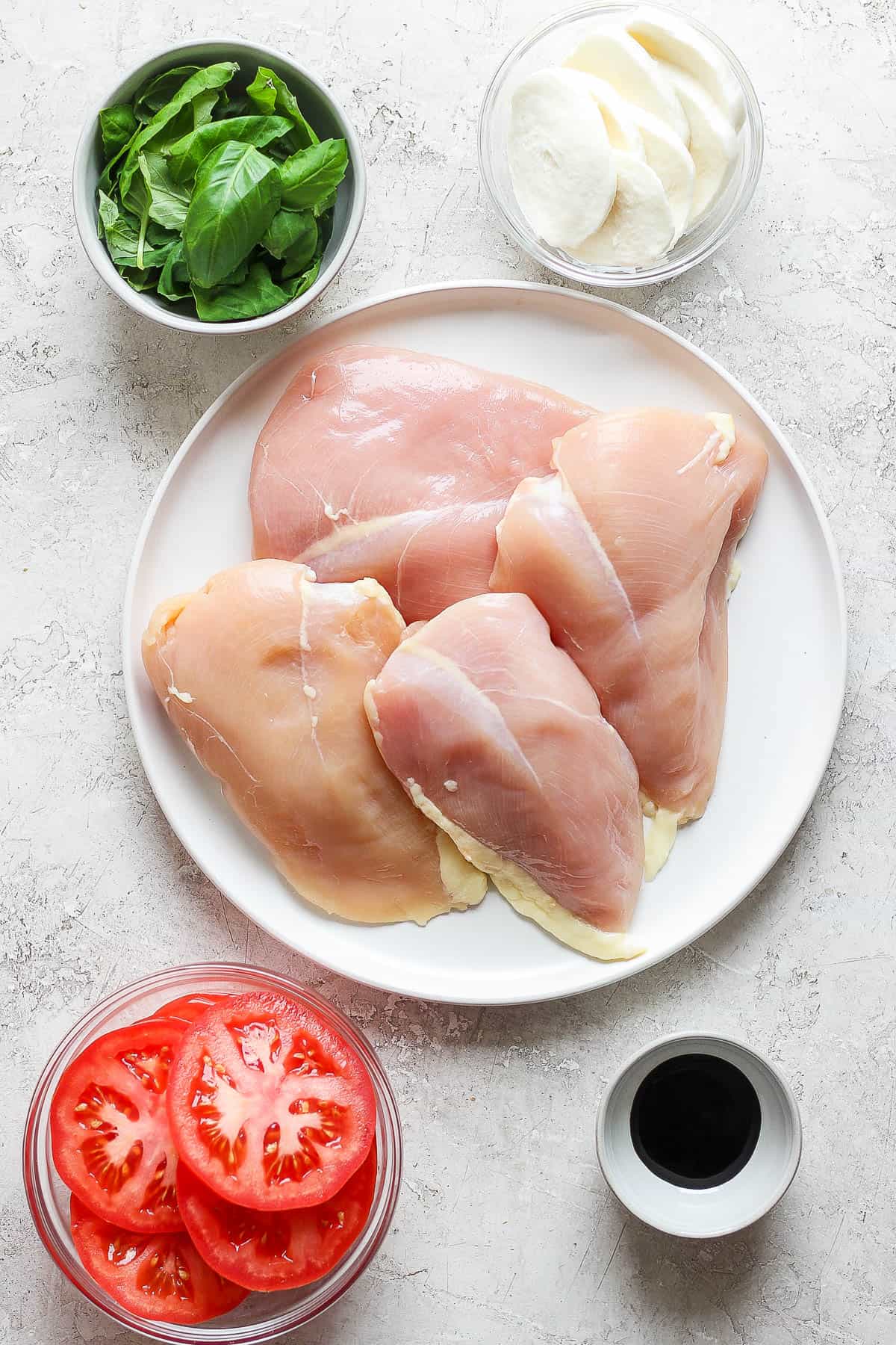 Ingredients for chicken caprese in separate bowls and plates.