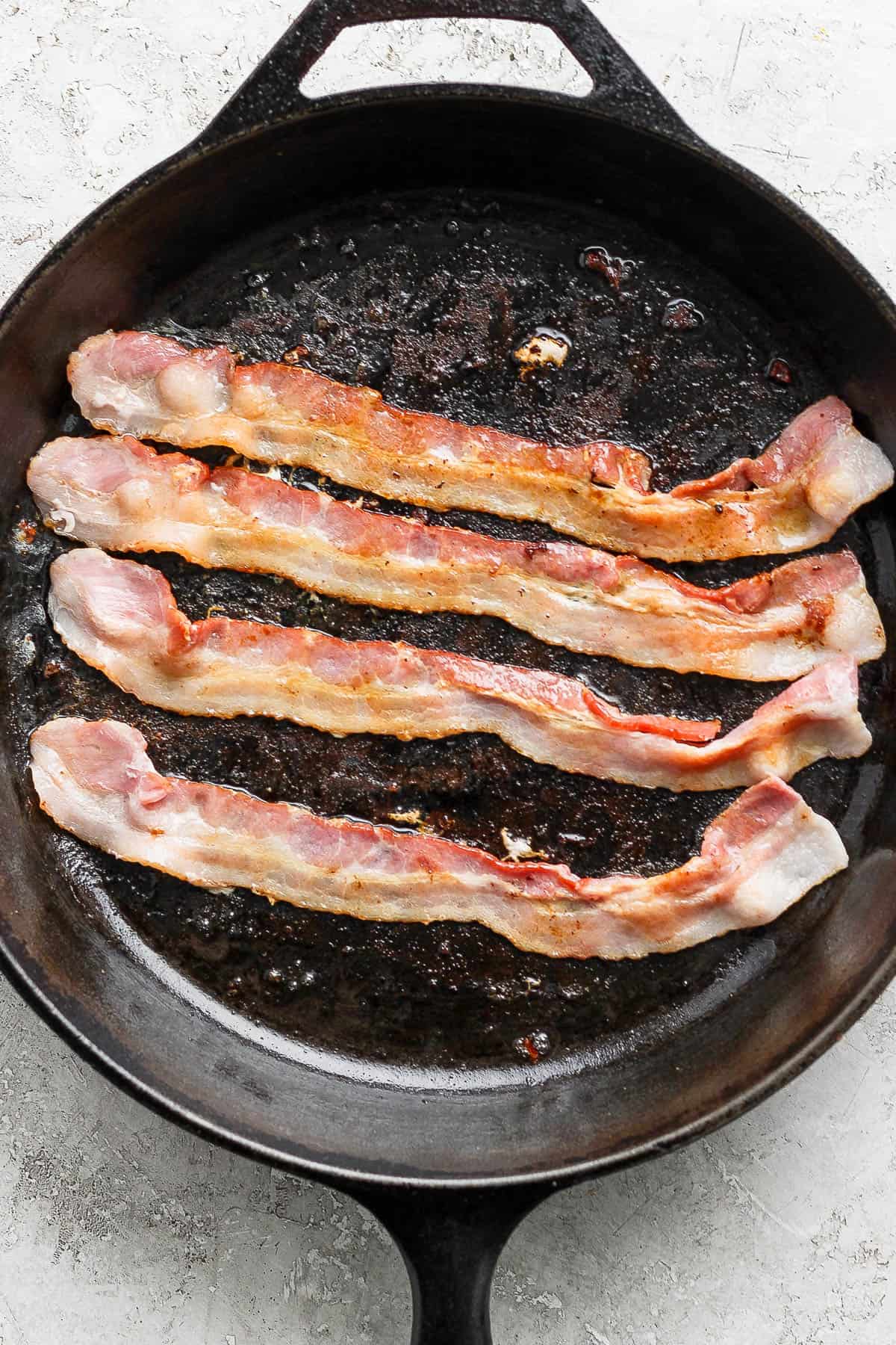 Partially cooked bacon in a cast iron skillet.