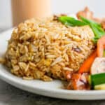 Side angle shot of a scoop of hibachi fried rice on a plate next to some veggies.