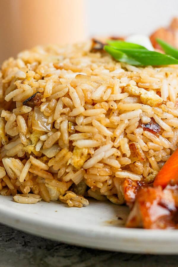 Side angle shot of a scoop of hibachi fried rice on a plate next to some veggies.