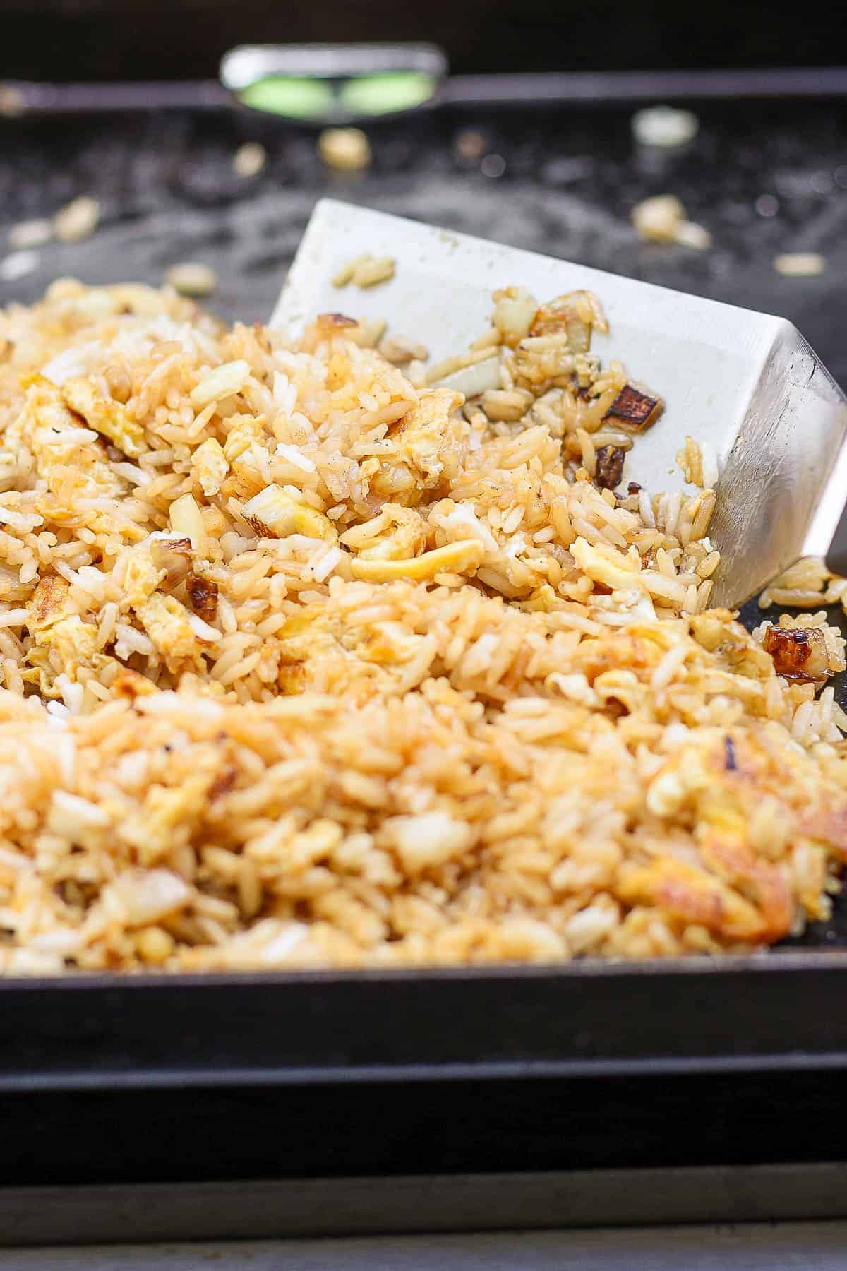 A large spatula moving around the fried rice on the cook top.