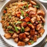 Top down shot of a big bowl of salmon fried rice with salmon chunks and rice with peas and carrots in it.