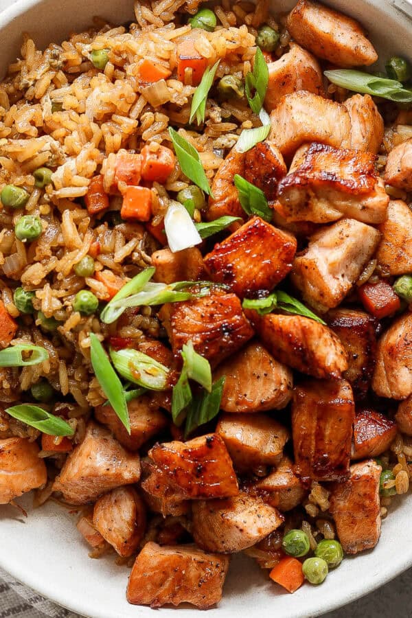 Top down shot of a big bowl of salmon fried rice with salmon chunks and rice with peas and carrots in it.