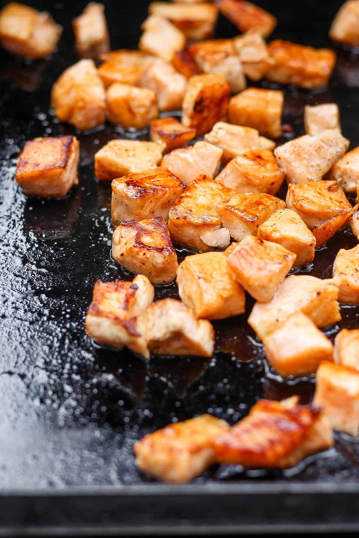 Marinated salmon pieces cooking on a griddle.