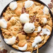 Top down shot of a skillet filled with a s'mores cookie with two scoops of ice cream on top and two spoons sticking out the side.