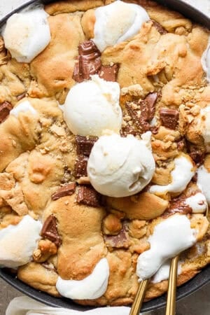 Top down shot of a skillet filled with a s'mores cookie with two scoops of ice cream on top and two spoons sticking out the side.