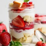 Straight on shot of a mason jar filled with a strawberry shortcake parfait with layers of pound cake, macerated strawberries and a whipped cream filling.