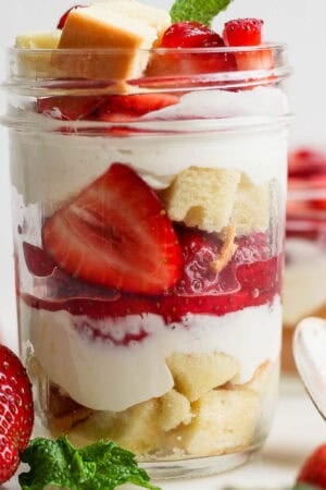 Straight on shot of a mason jar filled with a strawberry shortcake parfait with layers of pound cake, macerated strawberries and a whipped cream filling.