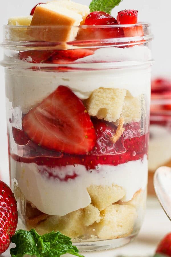 A mason jar filled with a strawberry shortcake parfait with layers of pound cake, macerated strawberries and a whipped cream filling.