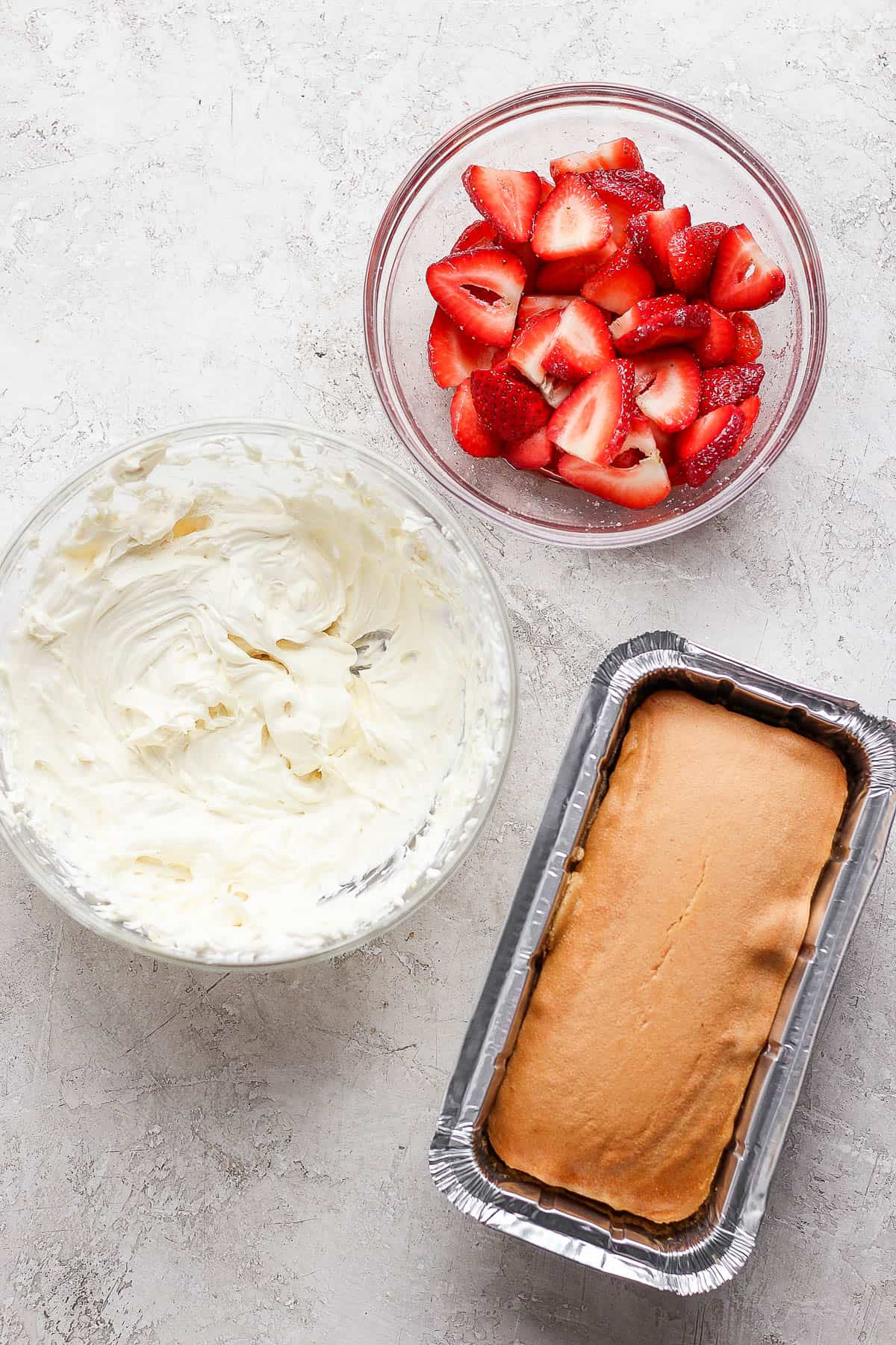 A bowl of macerated strawberries, whipped topping, and a pound cake.