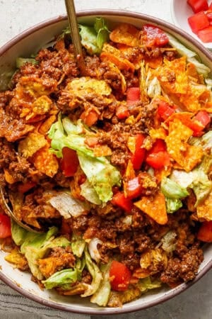 Top down shot of a bowl of homemade taco salad recipe with ground beef, cheese, chops and lettuce. Two spoons sticking out of the bowl.