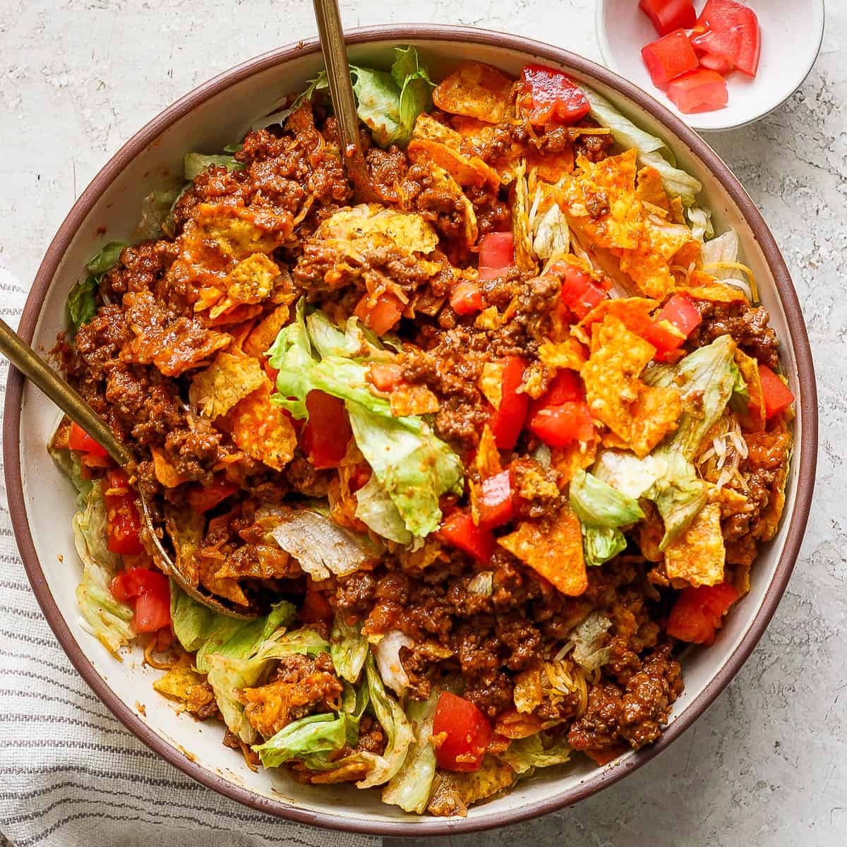 Top down shot of a bowl of homemade taco salad recipe with ground beef, cheese, chops and lettuce. Two spoons sticking out of the bowl.