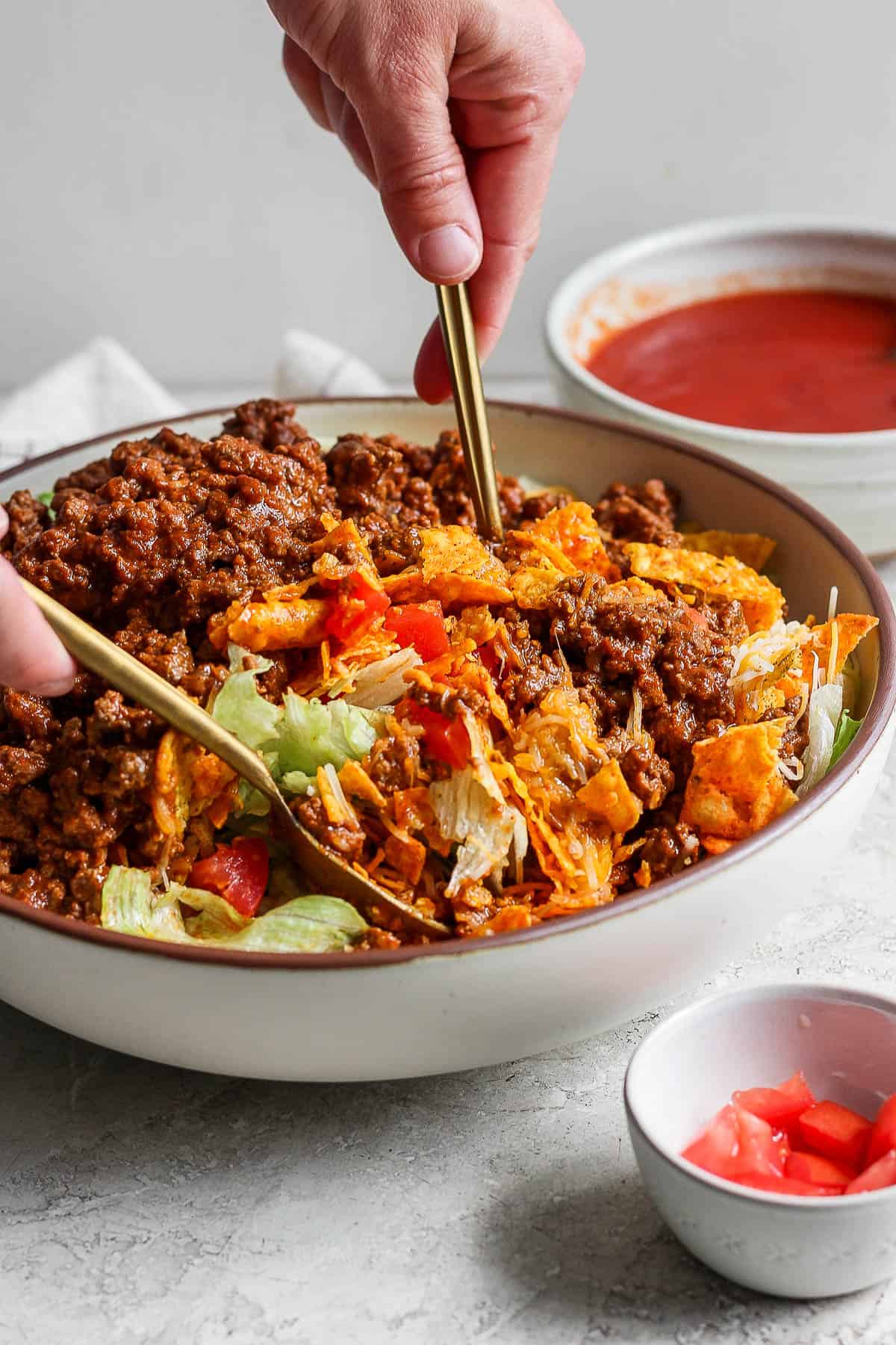 A large bowl of taco salad being mixed with two spoons.