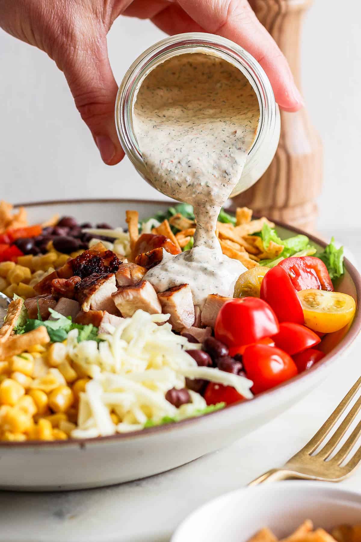 Chipotle ranch dressing being poured on the salad.