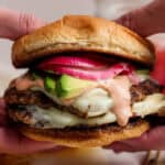 Someone holding a double-stacked turkey smash burger on a bun with burger sauce, avocado and quick-pickled onions.