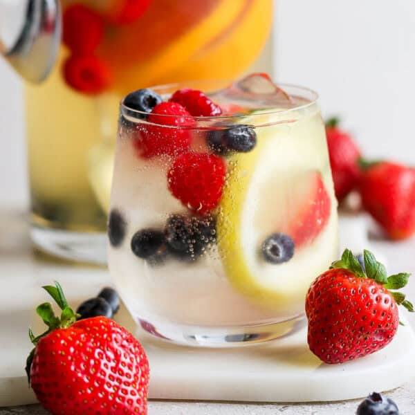 Straight on shot of a glass of white sangria with lemon, raspberries and blueberries.