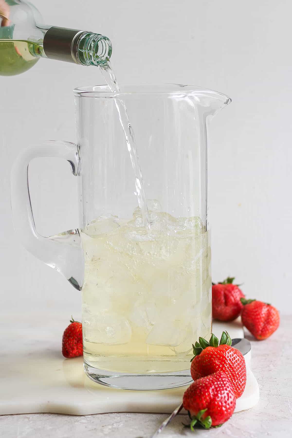 A bottle of wine being poured into a glass pitcher.