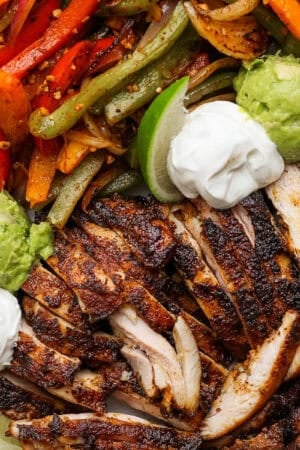 Top down close up shot of a small tray filled with Blackstone chicken fajitas, guacamole, sour cream and limes.