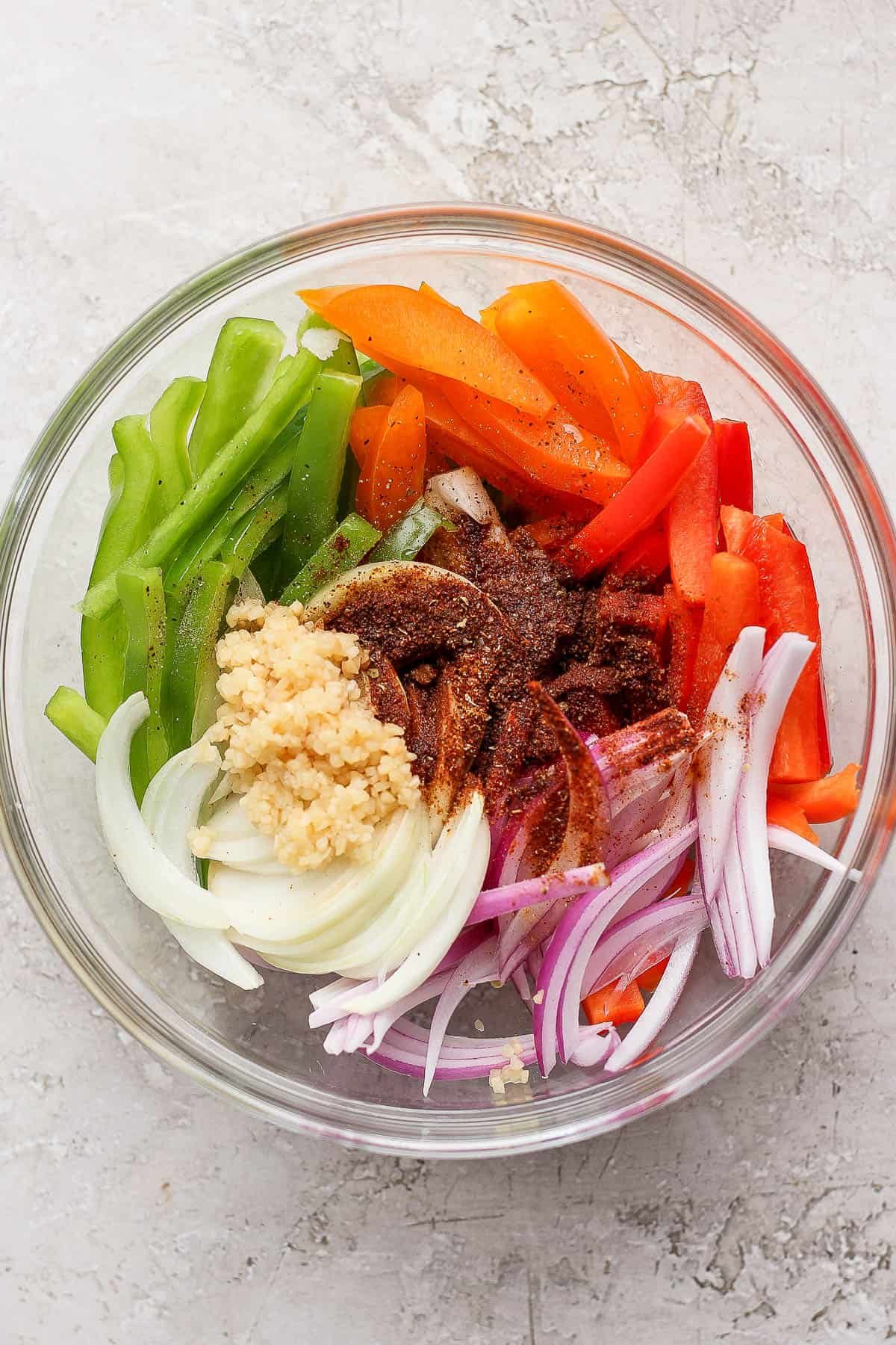 Fajita veggies and onions in a large bowl with seasoning and garlic.