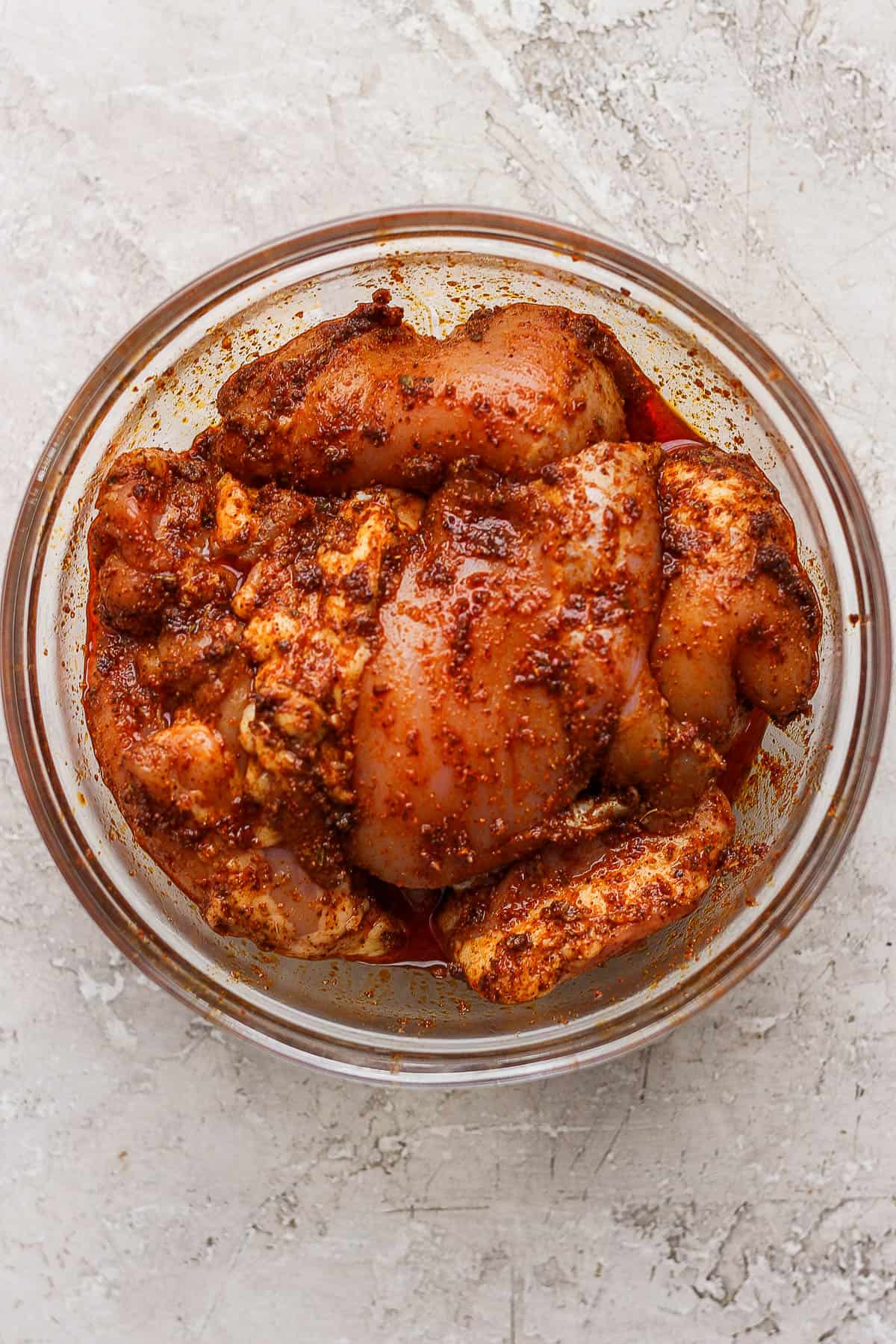 Chicken thighs marinating in a large glass bowl.